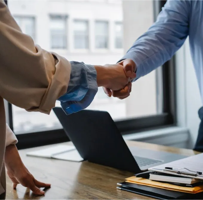 Twee mensen geven elkaar een hand boven een bureau
