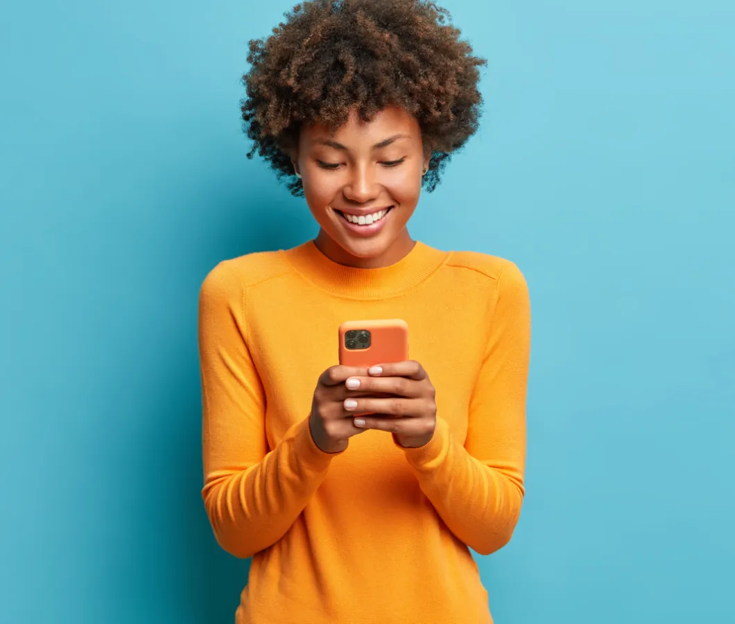 Lachende vrouw in gele trui kijkt op haar telefoon